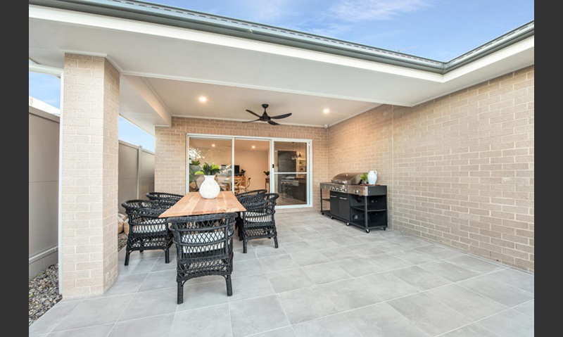 The outdoor dining area of a home designed with cream bricks and dark contrasted outdoor furniture.