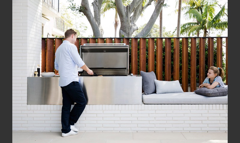 A family in the white brick designed outdoor kitchen space of their home.