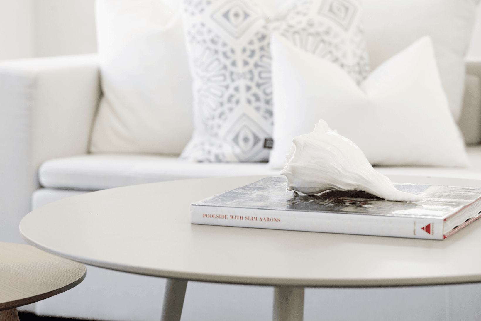 Coastal Hamptons styling with white couch, coffee table book and shell .