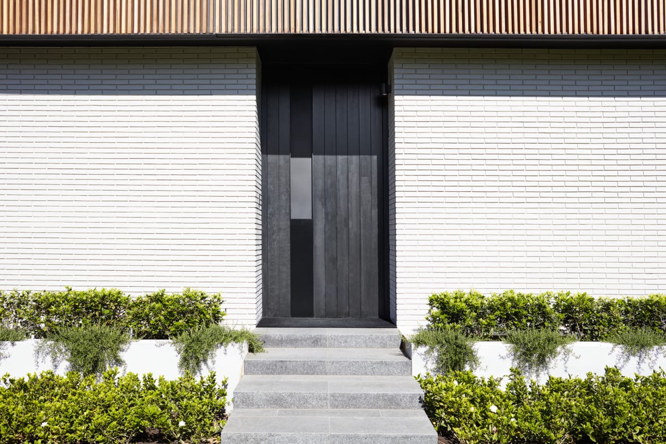 White brick home with black door and garden